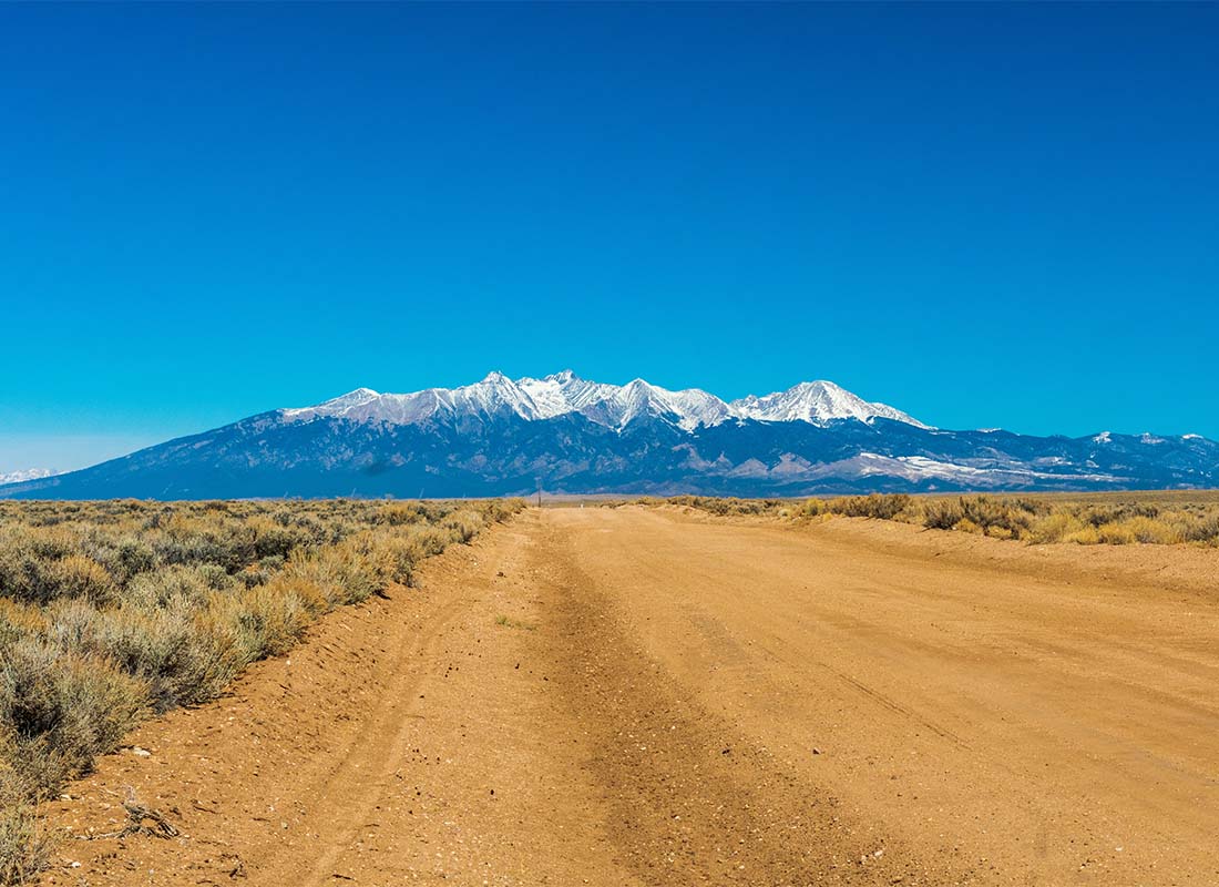 Alamosa, CO - Scenic View of Snow Capped Mountains Against a Bright Blue Sky with a Desert Field in the Front in Alamosa Colorado