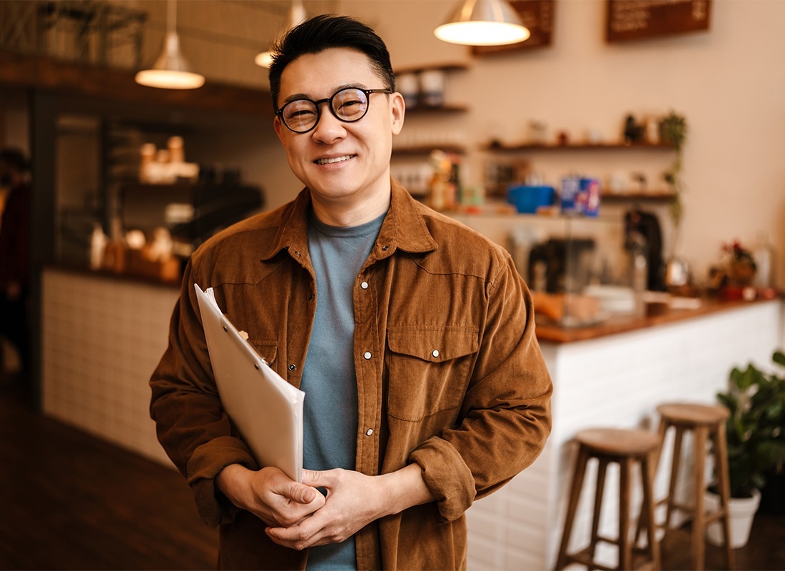 Business Insurance - Portrait of a Cheerful Middle Aged Businessman Holding Papers in his Hands Standing in his Small Main Street Cafe