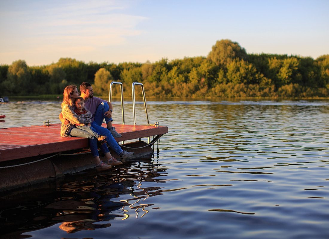 Contact - Portrait of a Young Family with a Son Sitting on a Wooden Dock by the Lake at Sunset Looking Out at the Water